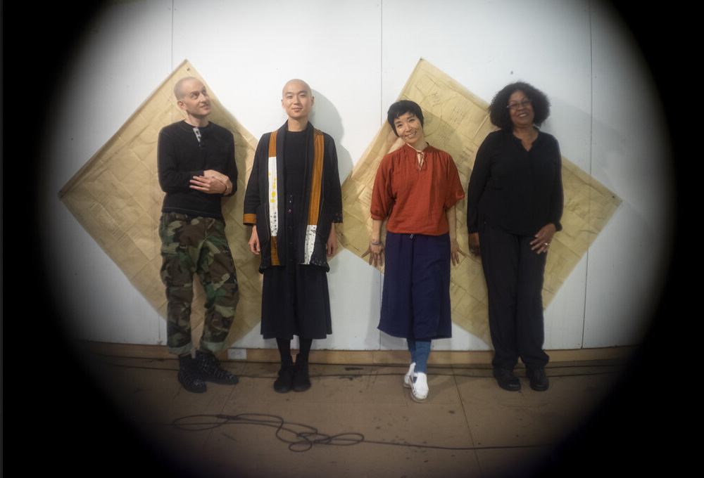 The four artists standing in a line in front of a wall